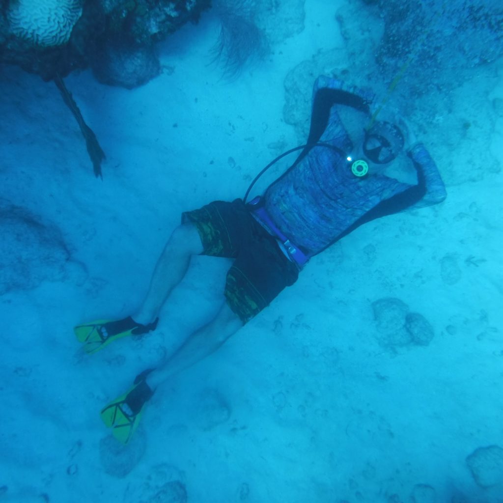 "A man lying on the surface underwater, posing while scuba diving. The image shows a diver in a relaxed and playful pose