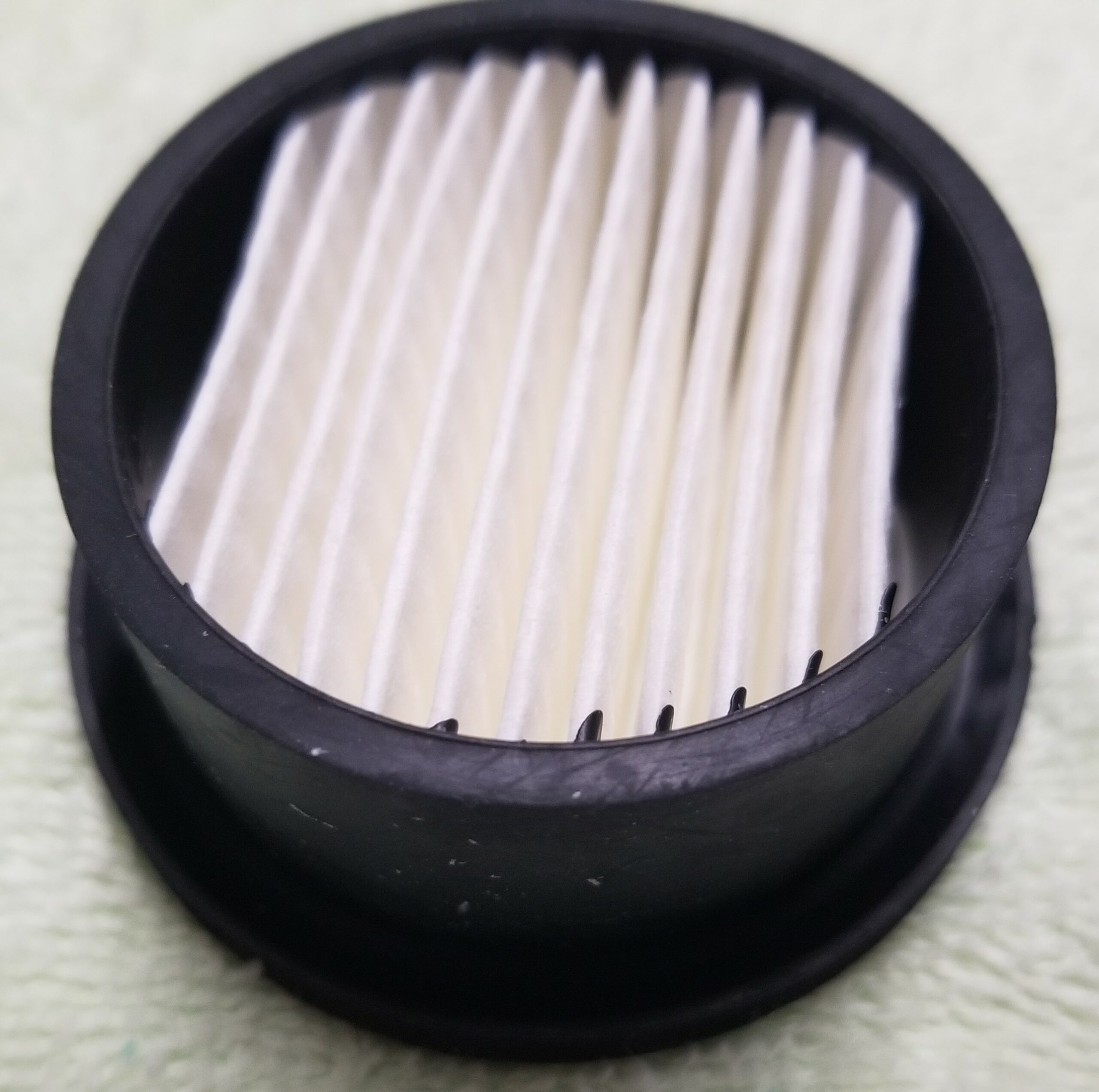 a white pleated filter in a black round frame on a textured surface.